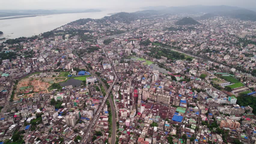 An aerial shot of a vast city with a river surrounded by hills under a cloudy misty sky.