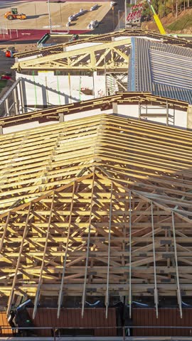 View of wooden roof trusses and blue waterproof membrane on a building under construction in Latvia.