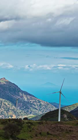 View of two wind turbines standing on a green hillside overlooking the sea under a cloudy sky, Latvia.