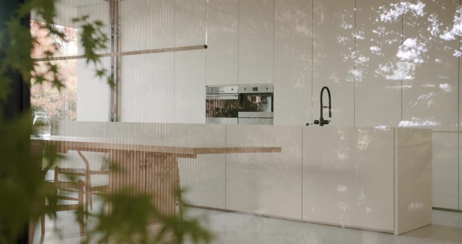 Modern Minimalist Kitchen Design with Island and Dining Table. Natural Light and Outdoor View Enhance the Serene Atmosphere. Stylish Interior with Clean Lines and Neutral Colors.