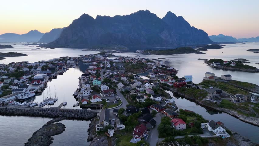 An Aerial view of the Norwegian fishing village of Henningvaer lit by the midnight sun, with mount festvaagtind in the background in Lofoten