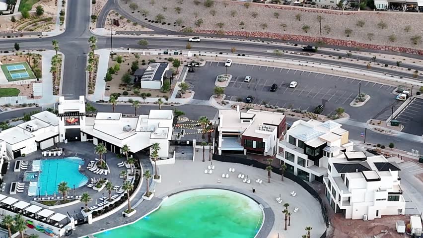 An aerial shot of white houses with a turquoise swimming pool and a large artificial lagoon, surrounded by roads and luxurious neighborhood