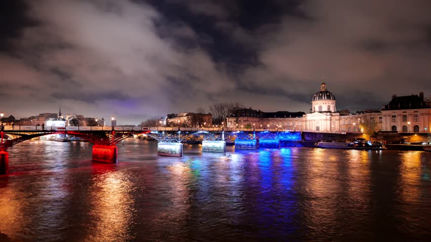 View of the illuminated Institut de France and Seine river with light trails from passing boats at night in Paris, Ile-de-France, France.