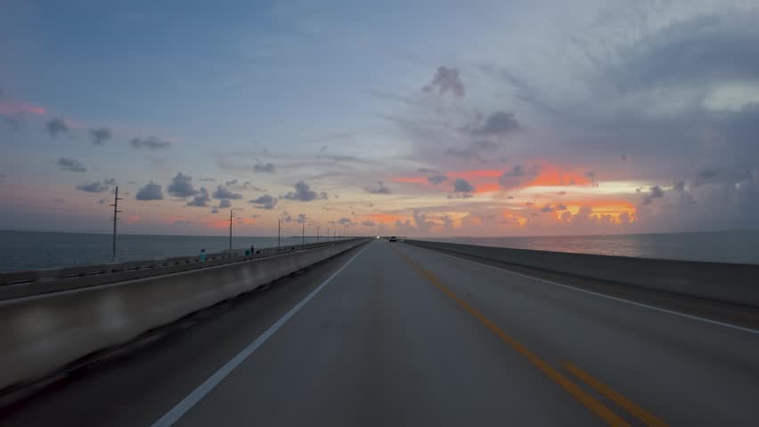 View of a car driving along the Overseas Highway over the ocean during a colorful sunset in Islamorada, Florida, United States.