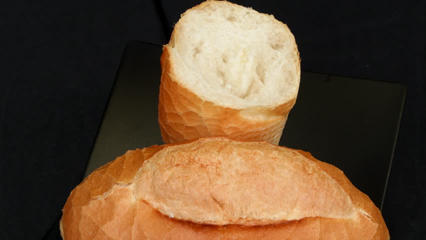 Close-up of Vietnamese plain banh mi bread broken in half on black plate.