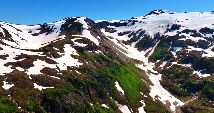 Mighty rocks covered with greenery and snow. Sun lights the beautiful mountains. Alaska wilderness.