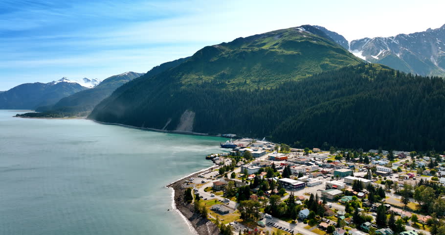 Residential area on the waterfront of the calm mountain river. Jaw-dropping verdant mountains around the town. Alaska. Aerial view.
