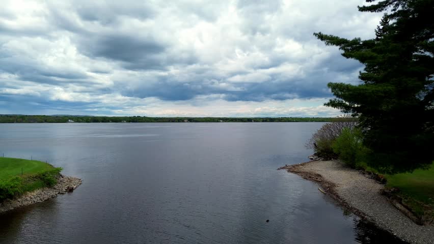 An aerial drone view of Ottawa River with distant wooded shoreline under cloudy sky in Canada