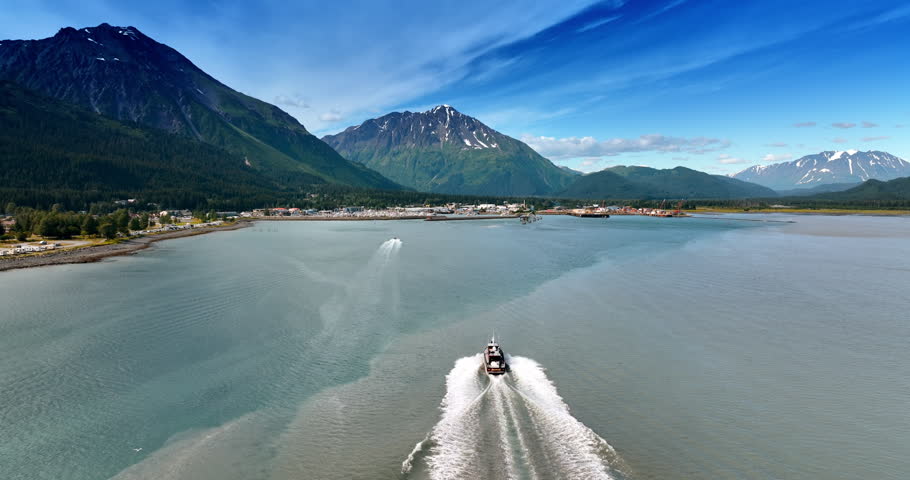 Following a motor boat moving by the waterscape to the town in Alaska. Wonderful mountain range at backdrop.