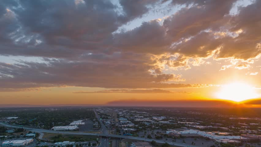 Aerial timelapse drone shot of a sprawling urban landscape during a vibrant sunset showing moving clouds above a suburban city center and major roadway intersection