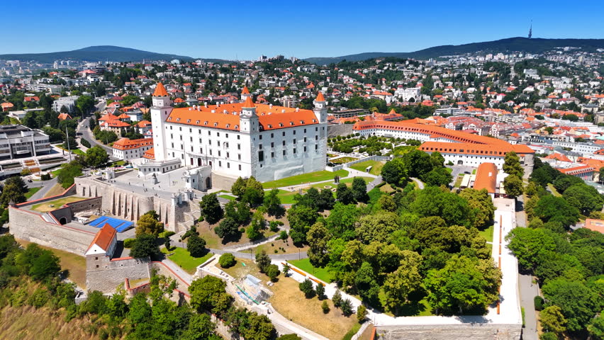 Approaching the building of the medieval Bratislava Castle. Green scenery of the city with landmark in the center. Aerial view.