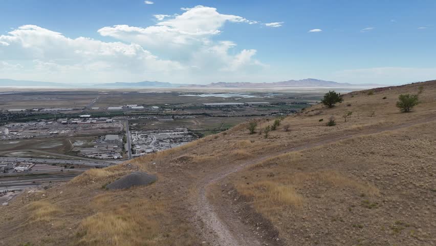 A drone shot of a terrain landscape featuring a large-scale mining operation on a hillside, with a highway under the clear sky