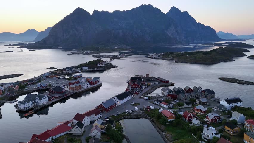 An Aerial view of the Norwegian fishing village of Henningvaer lit by the midnight sun, with mount festvaagtind in the background.