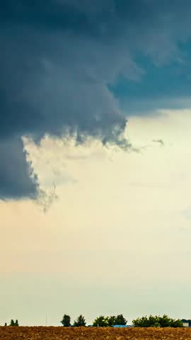 View of dark, heavy storm clouds gathering above a rural field in Latvia.