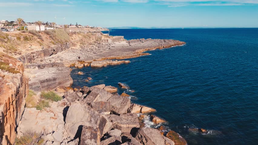 Establishing shot of the Atlantic Ocean with clear blue waters and rocky coastline in Estoril, Portugal.
