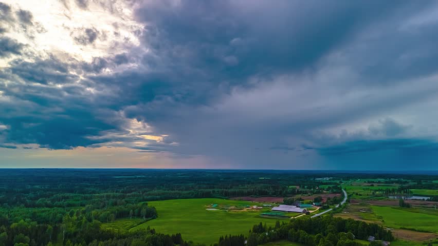 Aerial view of lush green fields and dense forests under a dramatic stormy sky in Latvia.