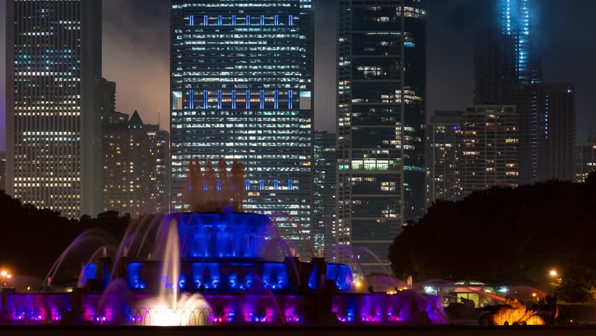 Chicago fountain at night showcases a mesmerizing timelapse of color changing water jets set against a stunning backdrop of illuminated downtown city office buildings