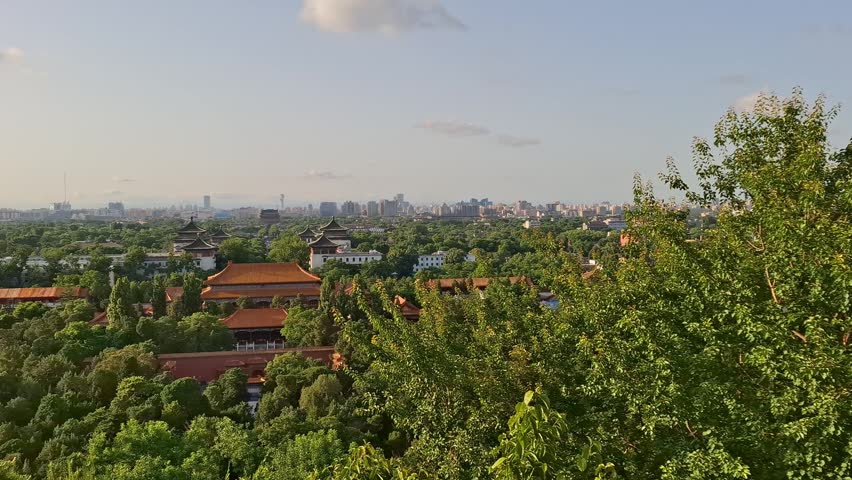 Scenic aerial view of the Forbidden City and Beijing from Jingshan Park. Ancient palace roofs, green park trees, city skyline.
