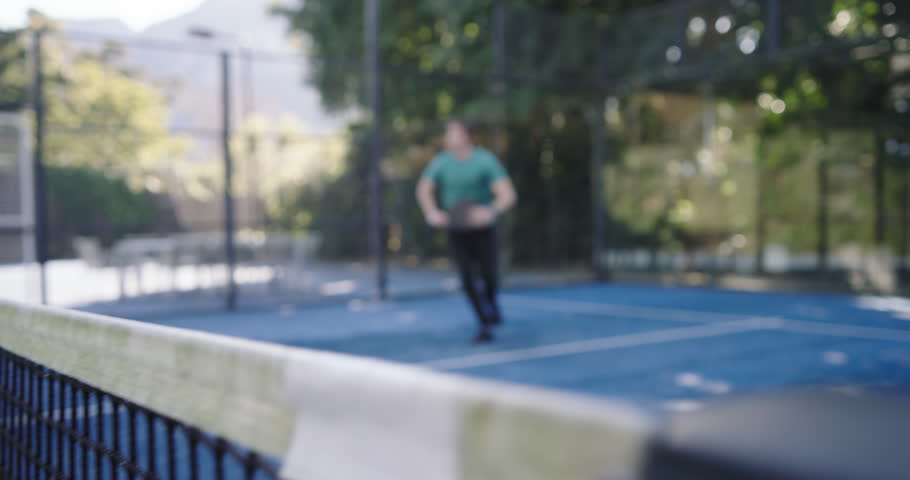 Diverse male team rushing to help teal-shirt player slipping after run on blue court holding paddle. Padel, teamwork, assist, recovery, outdoor, turf, camaraderie