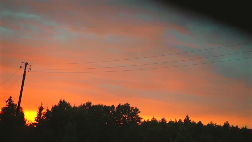 Vibrant orange sunset sky over dark forest silhouette from train window