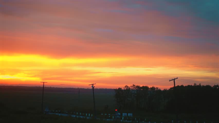 Vibrant orange sunset sky over dark forest silhouette from train window