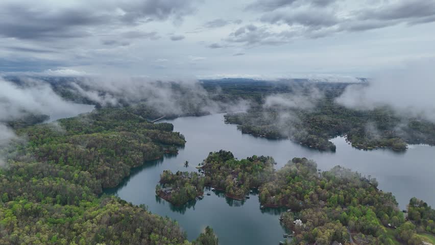 Aerial view of a lake and islands surrounded by lush forest and low-hanging clouds in Asheville, North Carolina, United States.