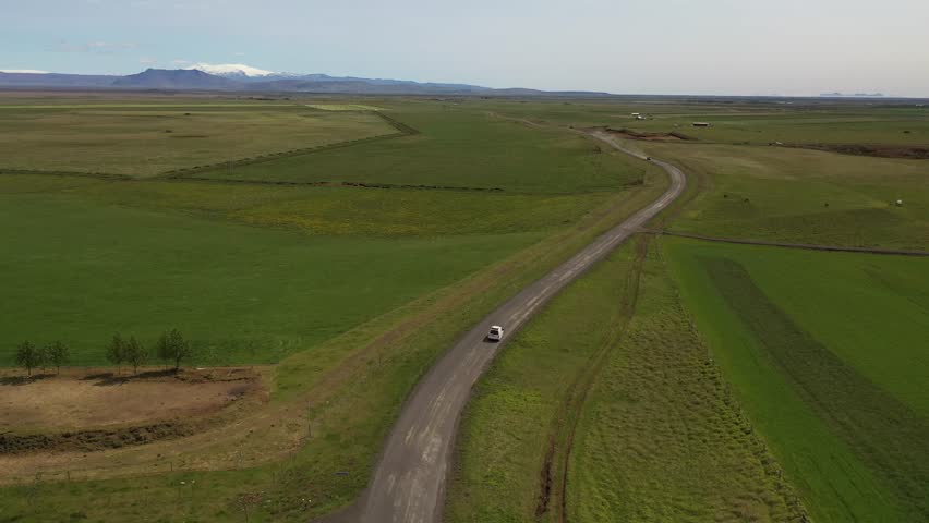 Aerial view of a car driving on a rural road through green fields in Hella, Rangarthing ytra, Iceland.
