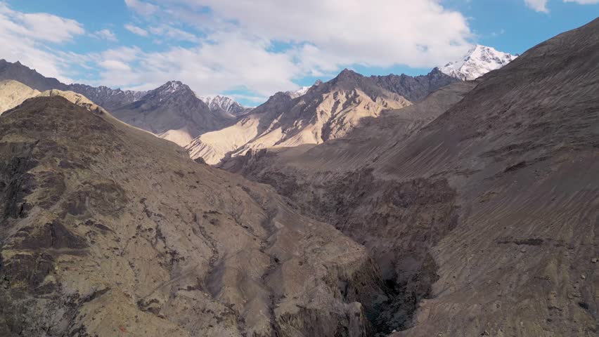 Aerial view of the rugged, arid mountain landscape of the Himalayas with deep valleys and rocky slopes under a blue sky with scattered clouds in Diskit, Ladakh, INDIA.