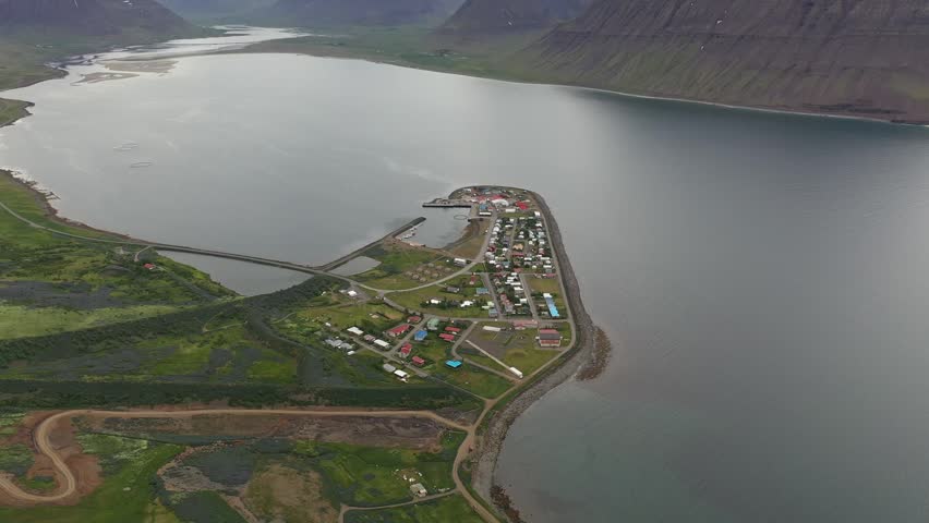 Aerial view of the village of Flateyri situated on a narrow spit of land extending into the fjord, surrounded by steep mountains and calm water in Flateyri, Isafjardarbaer, Iceland.