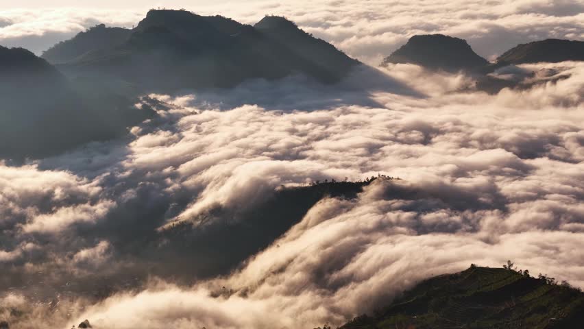 Aerial view of mountains rising above a thick sea of clouds during golden hour in Indonesia.