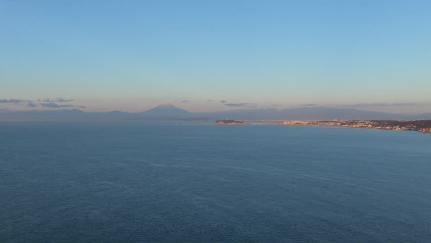 Aerial view of Mount Fuji rising above the calm ocean and the distant coastline of Japan.