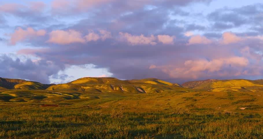 Stunning sunset clouds moving over a vibrant spring landscape with green and yellow rolling hills in California.