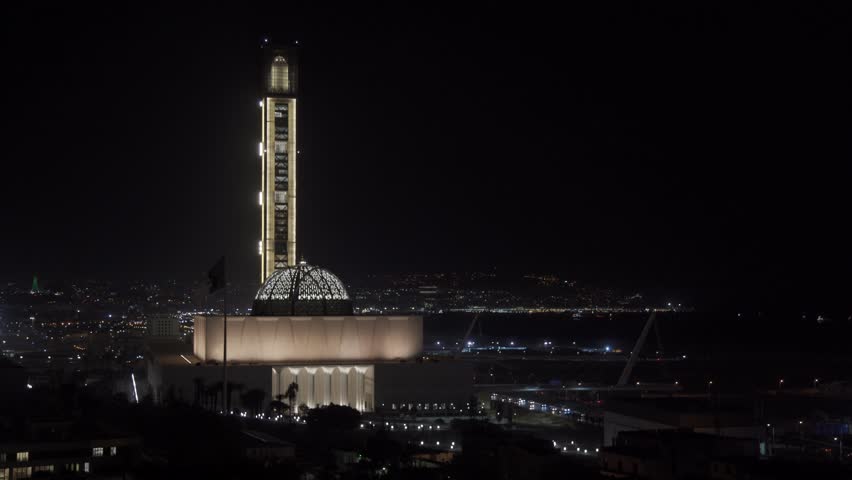 Aerial view of the illuminated Great Mosque of Algiers with city lights glowing in the background at night in Algeria.