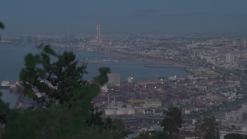 Aerial view of the port and the Great Mosque of Algiers illuminated at dusk, with city lights stretching along the coastline of Algeria.