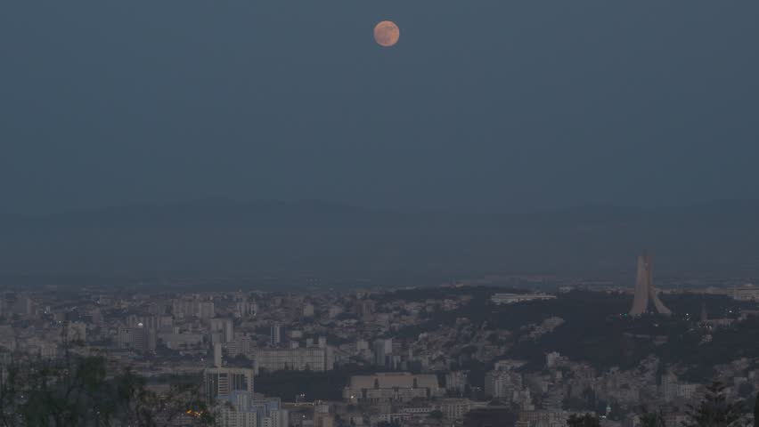 Aerial view of the Maqam Echahid monument overlooking the sprawling city skyline of Algiers under a full moon in Algeria.