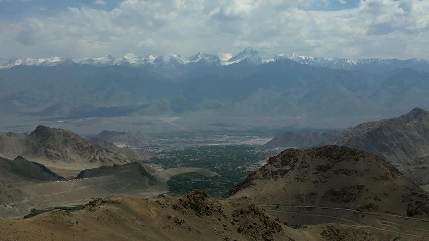 Aerial view of Khardung La pass with snow-capped Himalayan peaks and rugged mountain terrain under a cloudy sky in Khardung, Ladakh, India.