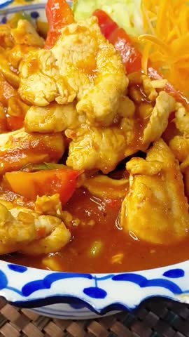 Rotating Plate of Chicken in Red Curry Sauce with Fresh Vegetables, Macro.
A detailed extreme close-up of a rotating blue-and-white patterned ceramic plate. The dish features tender slices of chicken coated in a glossy, rich red curry sauce, garnished with shredded fresh orange carrots and crisp white cabbage. The sauce catches the light as the plate spins. Shot in sharp focus with a shallow depth of field, natural studio lighting.