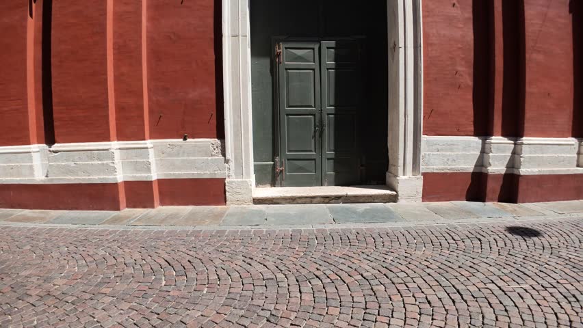 Red baroque facade of San Carlo Church in Modena, Italy, featuring a detailed stone architrave, vertical architectural elements, and a window under a clear blue sky on a bright sunny day
