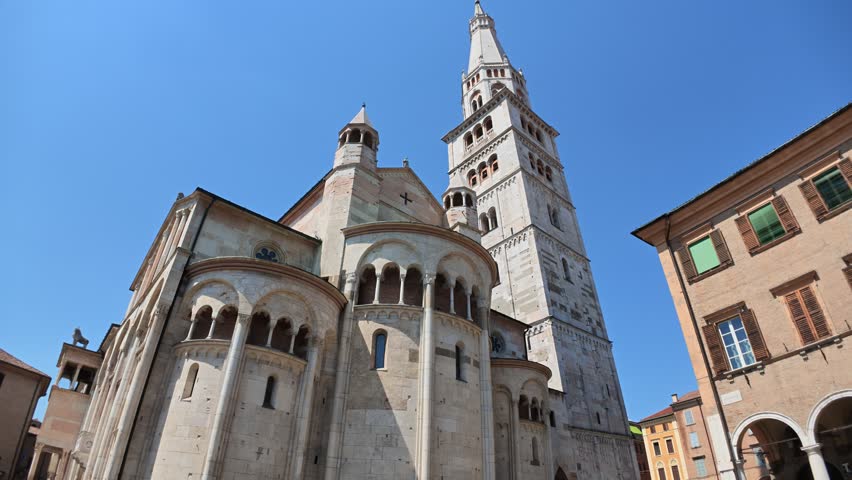 Panoramic view of the historical Modena cathedral and its iconic Ghirlandina tower under clear blue skies in downtown, in Piazza Grande square of Modena city in Italy