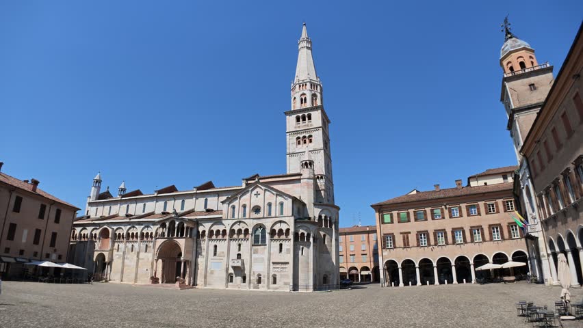 Modena Cathedral, a UNESCO World Heritage site, displaying its Romanesque architecture and the Ghirlandina Tower against clear blue sky, located on the historic Piazza Grandey of Modena city in Italy
