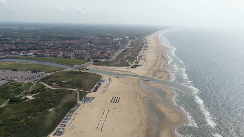 An aerial view of the sandy beach and inland waterway at Katwijk, South Holland, with the town stretching inland under a hazy sky