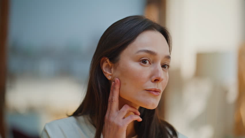 Lady inspecting face reflection gently touching smooth skin closeup. Middle-aged woman worried aging signs looking home mirror. Upset brunette dissatisfied facial texture at daily skincare routine.