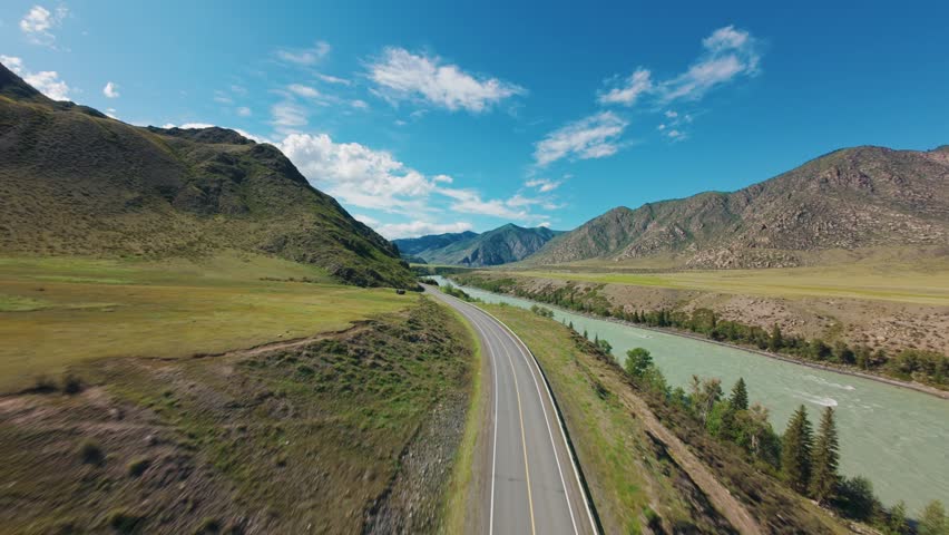 Aerial tracking shot of river and road winding through mountain valley with turquoise water and roadside trees Chuysky tract Altai, Siberia, Russia.