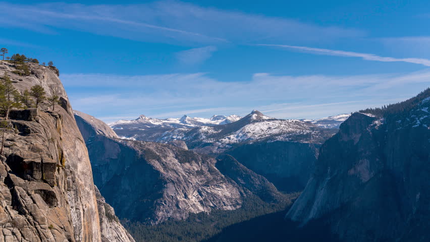A panoramic view of Yosemite Valley in California, showcasing its iconic granite cliffs and snow-capped mountains under a clear blue sky.