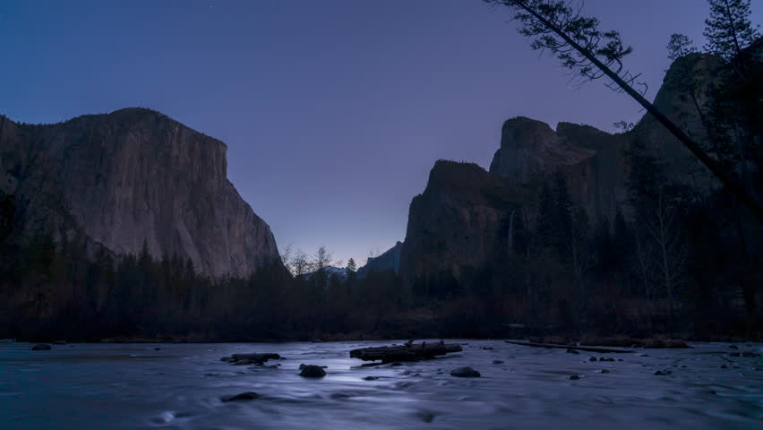 Yosemite Valley at dusk, with El Capitan and Bridalveil Fall visible in the distance, as the Merced River flows past.