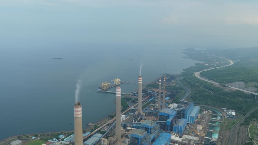 Massive coal fired power plant on the coast generating electricity, with smokestacks emitting smoke into the atmosphere near the sea