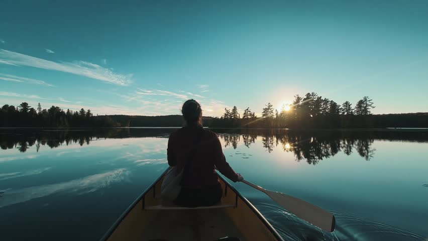 A slow-motion of Caucasian woman in the bow paddling across a calm backcountry lake on a beautiful morning in Ontario, Algonquin Park, Canada