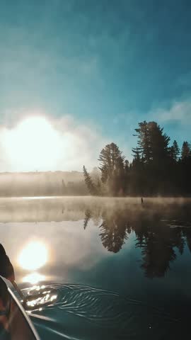 A slow-motion of Caucasian woman on a canoe in a calm backcountry lake with misty forest on a beautiful morning in Ontario, Algonquin Park, Canada