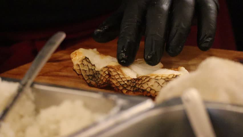 Close-up of a Chef in Black Gloves Placing a Piece of Seared Fish with Crispy Skin onto a Cutting Board