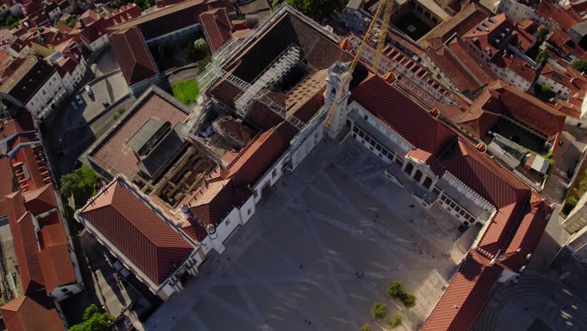 Aerial view of the historic Paco das Escolas courtyard at the University of Coimbra with surrounding red tile rooftops and a construction crane in Coimbra, Coimbra, Portugal.